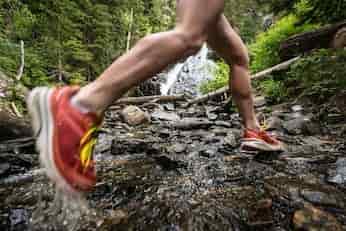 Running outdoors on rugged terrain near a waterfall, showcasing active fitness and wilderness adventure.